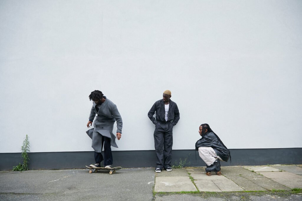 Group of three black and fashionable friends hanging out together outdoors with their skateboards and rollerskates